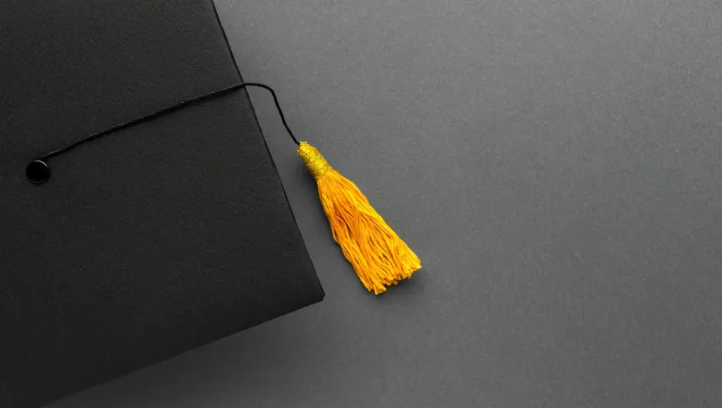 Black graduation cap with yellow tassel on gray background, symbolising achievement and success after getting University of Oklahoma scholarships.