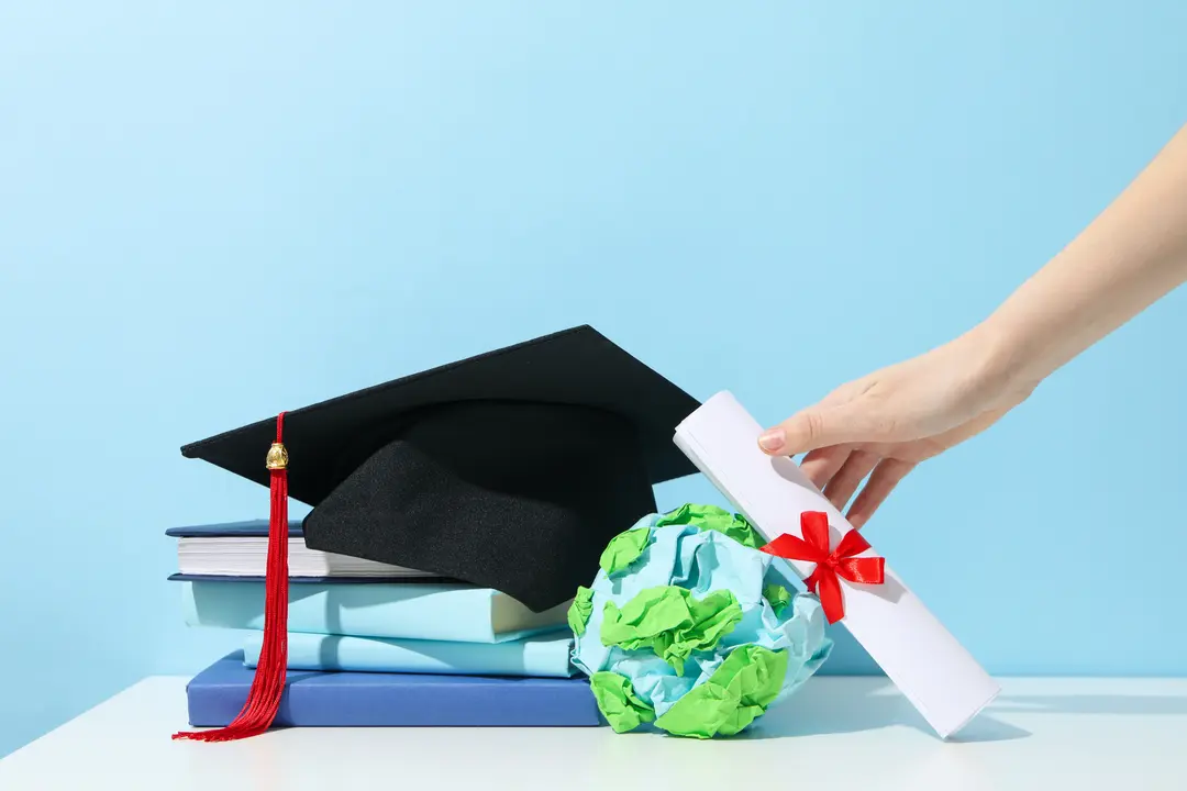 Abroad education loan without collateral: graduate hat keo on a heap of books and a hand holding university admission letter.